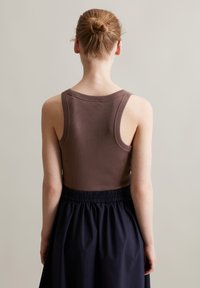 Braunes, geripptes Tanktop mit breiten Trägern, kombiniert mit einem dunkelblauen Rock mit elastischem Bund, von hinten betrachtet. Glatte Stofftextur.