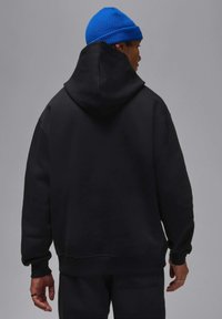 Felpa nera con ampio retro e cappuccio, realizzata in tessuto morbido. Accentuata da un berretto lavorato a maglia blu a contrasto. Vestibilità casual.