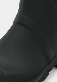 Botte en caoutchouc noire imperméable avec une texture lisse, un design épuré et un style bas. Comprend une semelle robuste pour une bonne adhérence.