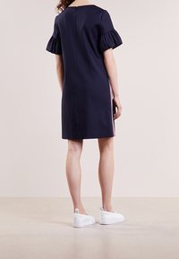 Vestido azul marino con mangas cortas y volantes, a la altura de la rodilla, con rayas rosas verticales a los lados. Combinado con zapatillas blancas.