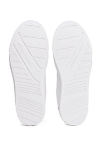 Einsame Paar weißer Schuhsohlen mit diagonalen und horizontalen Rillen, Markenname "Tommy Hilfiger" auf jeder Sohle eingeprägt.