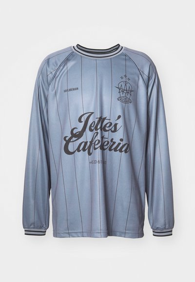 Jersey de manga longa azul claro com riscas verticais, gola e punhos pretos. Apresenta "Jette's Cafeteria" em letras negras em negrito.