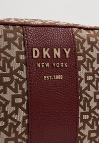 Brun och beige axelväska med en texturerad panel i vinröd färg, guld-tonat varumärke och ett upprepande DKNY-logomönster.