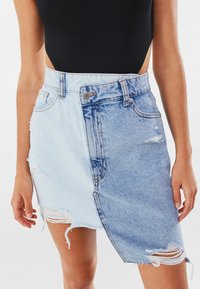 Farkkuhame vaalean- ja keskipsin sinisen sävyissä, epäsymmetrisellä muotoilulla, rispaantuneella helmalla ja kuluneilla yksityiskohdilla molemmilla puolilla.