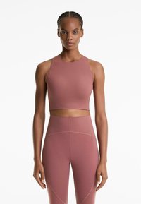 Woman standing straight wearing mauve high-neck crop top and matching high-waisted leggings against a white background.