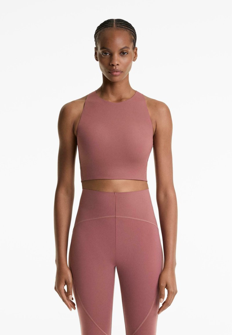 Woman standing straight wearing mauve high-neck crop top and matching high-waisted leggings against a white background.