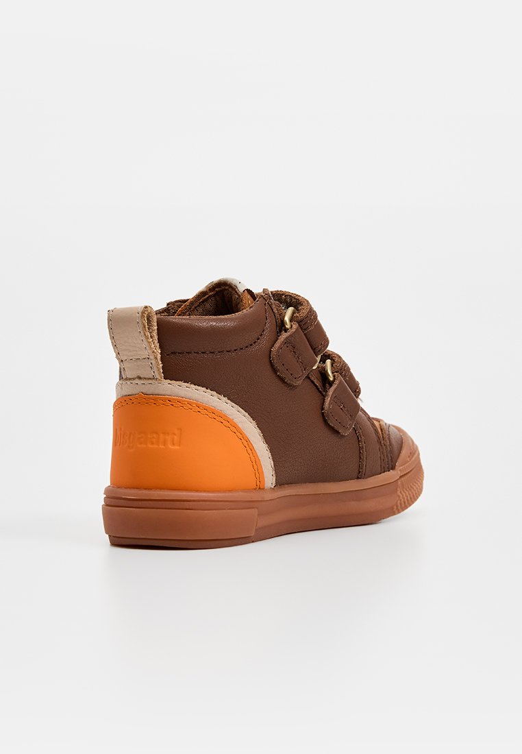 Bruine hoge sneaker met oranje accenten, dubbele klittenbandsluitingen, gestructureerd leer en rubberen zool, met een ronde neus en zachte kraag.