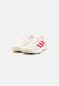 Vaaleanbeiget urheilukengät, joissa on verkkokangas päällisessä, valkoinen pohja ja punainen kolmen raidin muotoilu. Kenkässä on nauhat ja vetokahva kannassa.