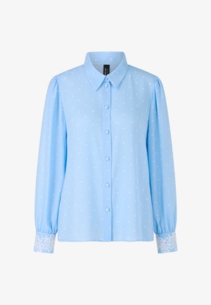 Hellblaue Bluse mit weißen Punkten, Knopfverschluss vorne, Kragen und langen Ärmeln. Die Manschetten sind mit detaillierten weißen Spitzenakzenten verziert.