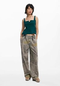 Turkos kort linnetopp med knappar, kombinerad med grå vida byxor med grafiska tryck. Plattformsskor med vävda remmar fulländar looken.