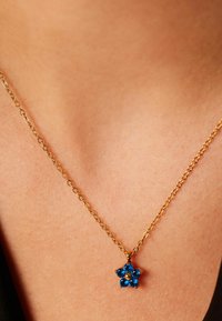 Gouden ketting met een blauwe edelsteen bloemhangertje met vijf bloemblaadjes, elk bezet met een ronde steen en een centrale gele edelsteen.