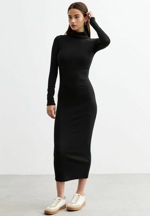 Robe à col roulé noir à manches longues, coupe cintrée, en tissu doux, atteignant le mi-mollet, associée à des baskets blanches et beiges.