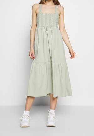 Lysegrøn midi-kjole med firkantet halsudskæring, brede stropper, blomsterbroderi på overdelen og lagdelt nederdel. Styled med hvide sneakers.