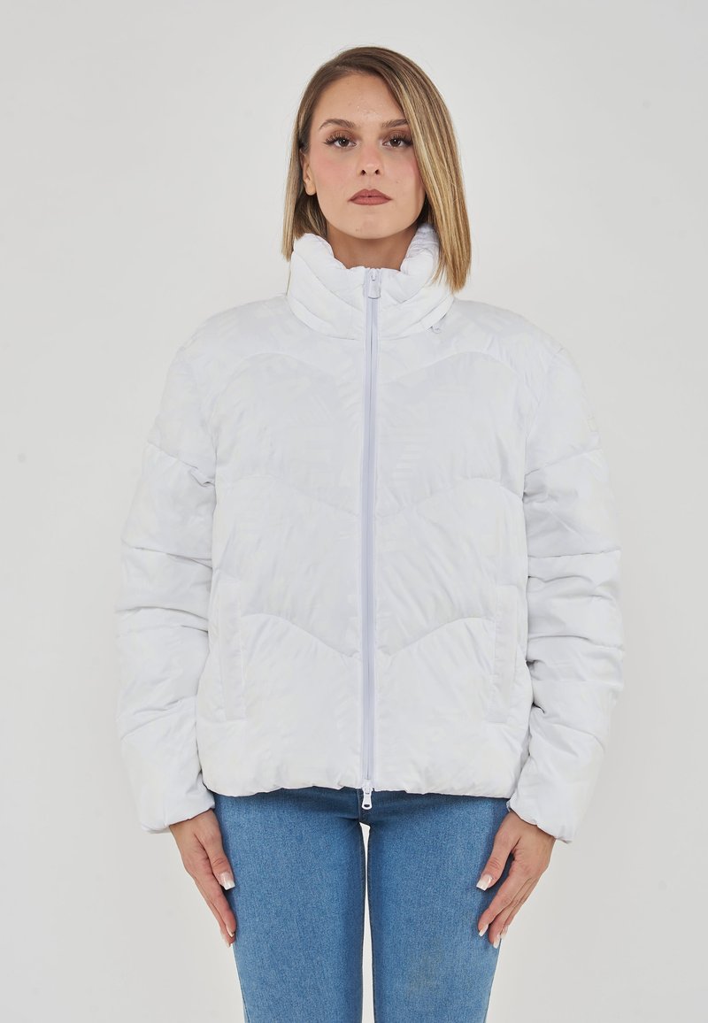 Giacca puffa bianca con collo alto, chiusura a zip e superficie testurizzata con un motivo sottile. Abbinata a jeans blu.