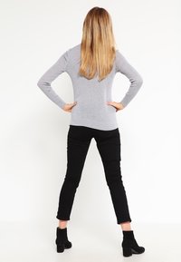 Šedý svetr s těsným siluetam, kombinovaný s černými slim-fit kalhotami a kotníkovými botami. Modelka má dlouhé rovné vlasy a je otočená zády k fotoaparátu.