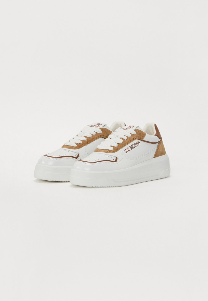 Sneaker bianche e beige con suola piattaforma, materiali in pelle e suede, punta rotonda e un logo prominente di lato.