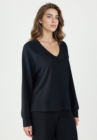 Czarna bluzka z długim rękawem w kształcie V, wykonana z miękkiego materiału. Posiada luźny krój oraz prążkowane akcenty wzdłuż dekoltu i mankietów.
