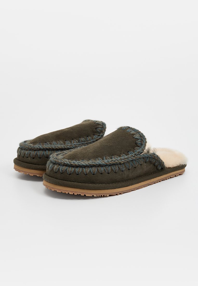 Bruine suede slippers met blauwe stiksels, pluizige crèmekleurige voering en rubberen zolen. Ronde vorm, open achterkant ontwerp. Geen zichtbare logo's.