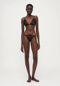 Svart undertøy i blonder med en bralette med bølgete kanter og matchende truse, begge med delikate blomsterønstre.