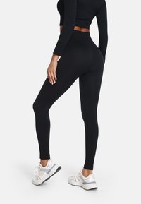 Čierne legíny s vysokým pásom vyrobené z hladkého, pružného materiálu. V kombinácii s bielymi športovými teniskami s šedými akcentmi a štruktúrovanou podrážkou.