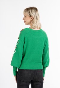 Maglione verde a maglia con orlo a coste e maniche a palloncino. Presenta accenti dorati decorativi lungo le maniche. Tessuto testurizzato e caldo.