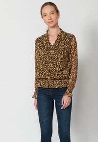 Blusa a maniche lunghe nera con motivo floreale caratterizzato da fiori gialli, arancioni e bianchi. Scollo a V e dettaglio arricciato in vita.