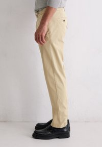 Beige Baumwollhose mit geradem Schnitt und seitlichen Taschen, kombiniert mit schwarzen Lederschuhen. Minimalistisches Design mit einfarbigem Muster.