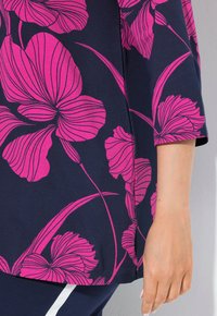 Navyfarbener Stoff mit großem rosa Blumenmuster und kräftigen Konturen; sichtbares gespaltenes Saumdetail. Glatte Textur, lässige Passform der Ärmel.