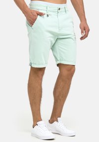 Ljusgröna bomullsshorts med uppvikt kant, framfickor och knäppning, i kombination med vita sneakers. Kort längd.