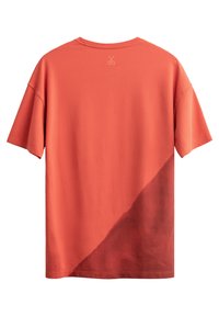 T-shirt à manches courtes en corail avec un dégradé diagonal bordeaux. Fabriqué en matériau doux, il présente un petit logo de ciseaux au dos du cou.