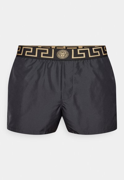 Čierne plavky s elastickým pásom, na ktorých je zlatý grécky kľúčový vzor a centrálny zlatý emblem. Hladká, ľahká tkanina.