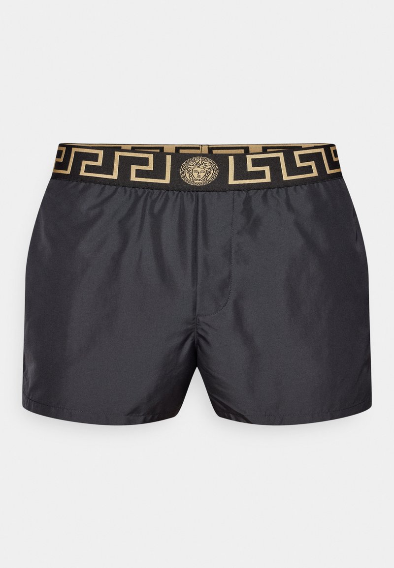 Costume da bagno nero con vita elasticizzata, in carattere greco dorato e un emblema centrale dorato. Tessuto liscio e leggero.