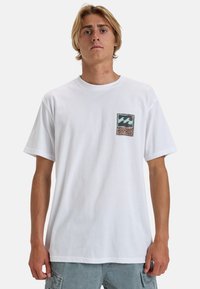 White cotton t-shirt featuring a small square logo with waves in blue and orange. Short sleeves and a crew neckline. Relaxed fit.