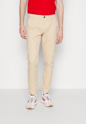 Chino en coton beige avec une coupe slim et des poches avant. Associé à des baskets blanches avec des accents rouges et bleus.