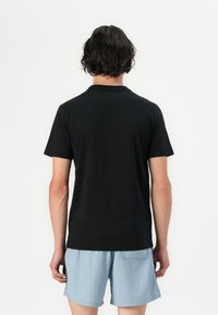 T-shirt noir à manches courtes en coton, avec un col rond, une coupe décontractée et un design simple, porté avec un short bleu clair.