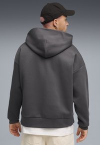 Grijze pullover hoodie met een ruime capuchon, drop schouders en een zachte textuur. Gecombineerd met een witte T-shirt en lichtgekleurde broek.