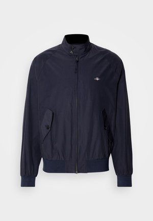 Sötétkék széldzseki magas gallérral, cipzáras záródással és két gombos oldalzsebbel. Sima textúra és rugalmas mandzsetták.