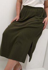 Olive green midi skirt with a textured finish, featuring an elastic waistband and a side slit for ease of movement.