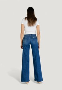 Korkeavyötäröiset siniset leveälahkeiset farkut, joissa on sileä pinta, kaksi takataskua ja näkyvä merkkilappu vyötäröllä.