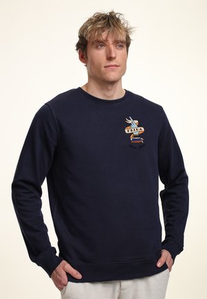 Granatowy sweter wykonany z miękkiego materiału, z okrągłym dekoltem, długimi rękawami oraz kolorowym haftowanym wzorem po lewej stronie klatki piersiowej.