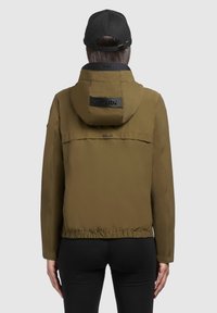Giacca leggera verde oliva con cappuccio aderente, vita elastica e patch logo nero. Tessuto morbido, maniche lunghe e design casual.