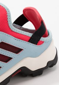 Sininen ja punainen urheilusandaali, jossa on teksturoitu verkkopinta, vahva kumipohja ja pehmustettu kantapään tuki, jossa on vetotuki.