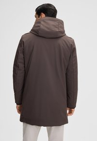 Bruine, waterdichte parka met een grote capuchon, een gladde textuur en een lange lengte. Heeft een minimalistisch ontwerp, zijzakken en naaddetails.