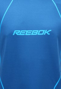 Camisa atlética azul com o logo da Reebok em azul-claro, feita de um tecido suave com detalhes em contraste ao longo das costuras.