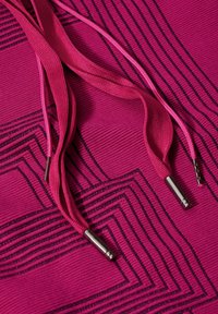 Rosa Textil mit schwarzen Linienmustern, versehen mit rosa Schnürsenkeln mit metallischen Spitzen, und weist eine strukturierte Oberfläche und geometrisches Design auf.