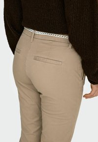 Beežid kitsad püksid tagumiste taskutega, kantud tumepruuni kootud kampsuni ja valge punutud vööga siniste aktsentidega.