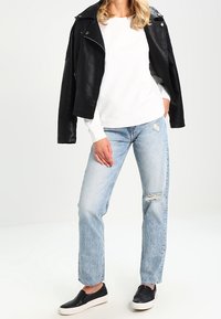 Chaqueta de motociclista de cuero negra sobre un suéter blanco texturizado, combinada con jeans rasgados de color azul claro y zapatos slip-on negros.