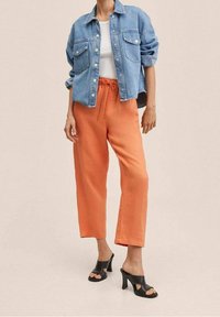 Denim jacket with pockets, white t-shirt, orange drawstring trousers, and black high-heeled sandals. Smooth textures and casual fit.