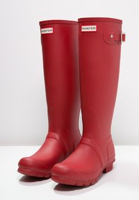 Bottes de pluie en caoutchouc rouge avec une finition brillante, hauteur mi-mollet, semelles texturées et détail de boucle sur le côté avec la marque "HUNTER".