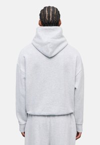 Felpa con cappuccio grigio chiaro, con un cappuccio grande e strutturato, vestibilità comoda e polsini a costine. Caratterizzata da un tessuto morbido e testurizzato e da un design minimalista.